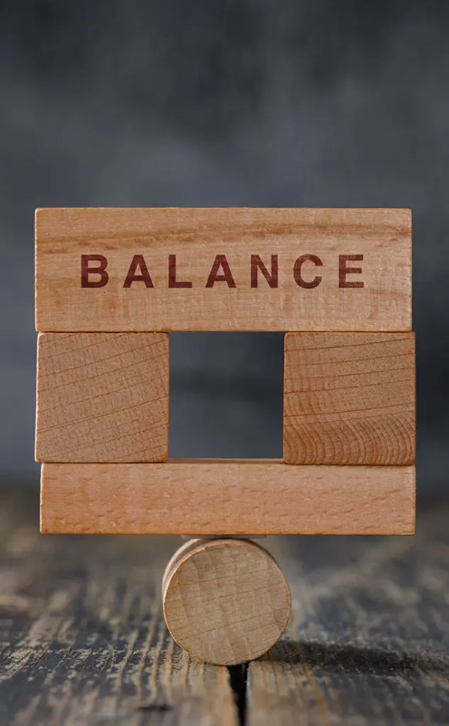 cubetti di legno con la scritta "balance" posti uno sopra l'altro in equilibrio su un pezzo di legno cilindrico